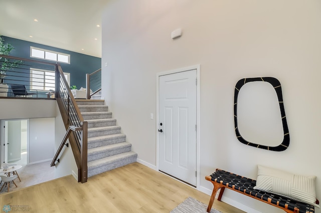 foyer with recessed lighting, a high ceiling, baseboards, stairs, and light wood finished floors