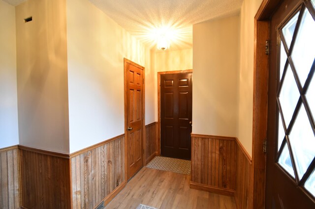 doorway featuring light wood finished floors, a wainscoted wall, and wooden walls