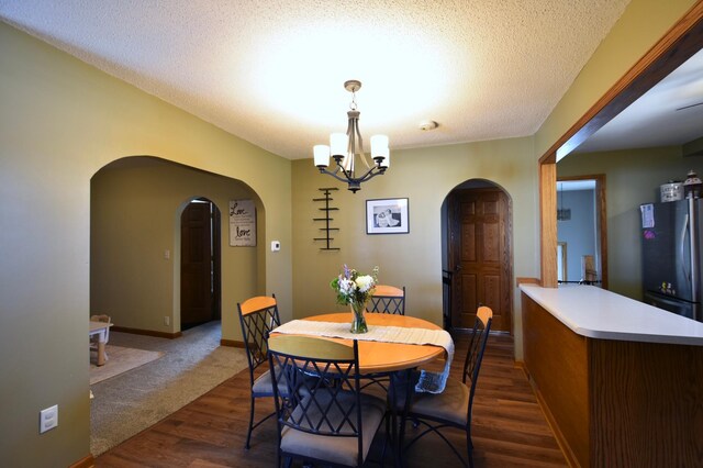 dining area with an inviting chandelier, arched walkways, baseboards, a textured ceiling, and dark wood-style flooring