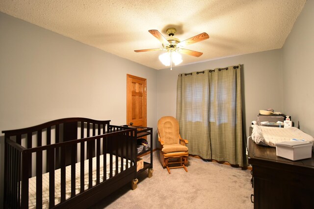 bedroom featuring a nursery area, carpet floors, a ceiling fan, and a textured ceiling