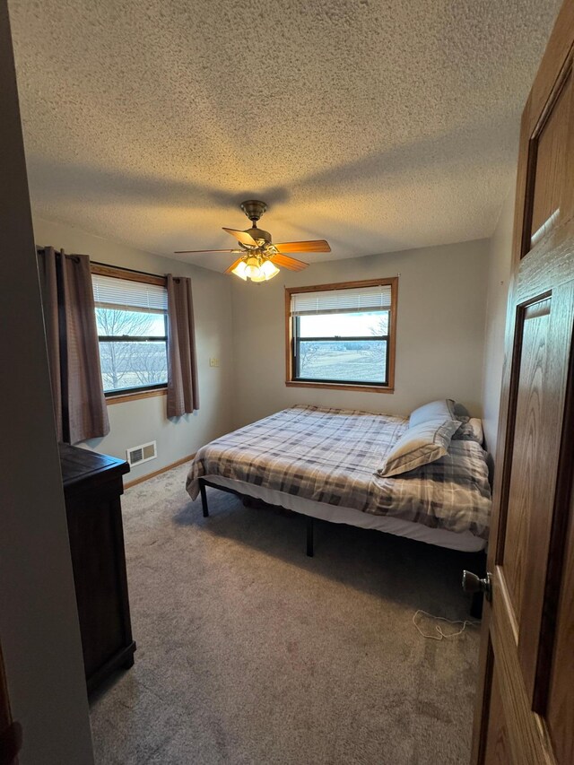 bedroom featuring ceiling fan, a textured ceiling, visible vents, and carpet