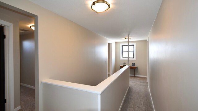 hall featuring baseboards, carpet floors, and an upstairs landing