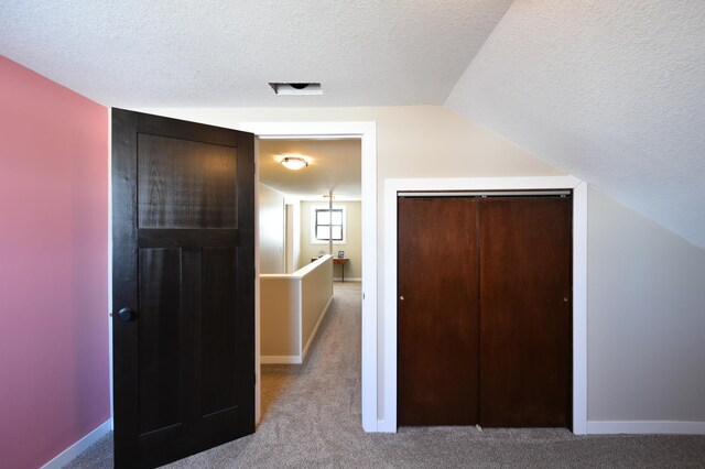 interior space featuring baseboards, vaulted ceiling, carpet flooring, and a textured ceiling