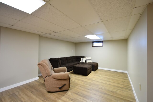 living room featuring light wood finished floors, a drop ceiling, and baseboards
