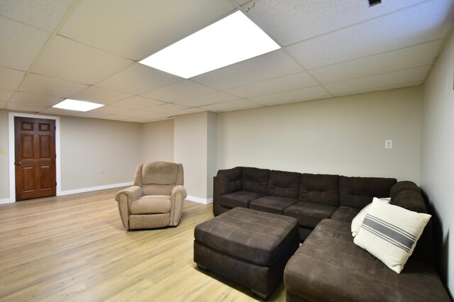 living room with light wood-style floors, a paneled ceiling, and baseboards