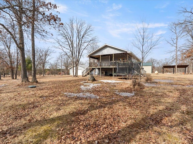 rear view of property featuring a wooden deck, stairs, a trampoline, and a detached carport