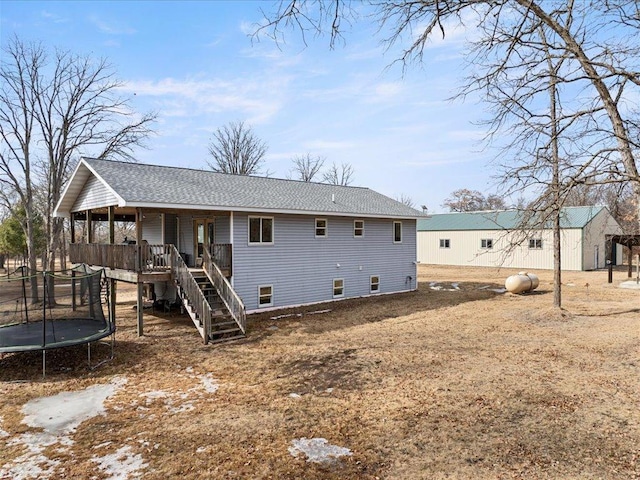 back of property with stairway, a shingled roof, covered porch, and a trampoline
