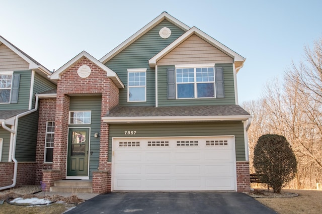 traditional-style home with an attached garage, roof with shingles, aphalt driveway, and brick siding