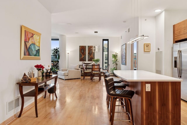 kitchen with light wood finished floors, visible vents, a kitchen breakfast bar, and stainless steel refrigerator with ice dispenser