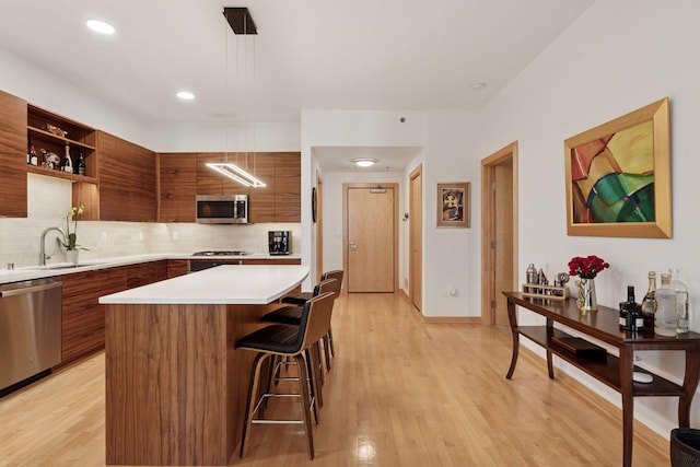 kitchen with modern cabinets, appliances with stainless steel finishes, brown cabinetry, and light countertops