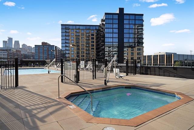 pool with a patio area, a city view, a community hot tub, and fence