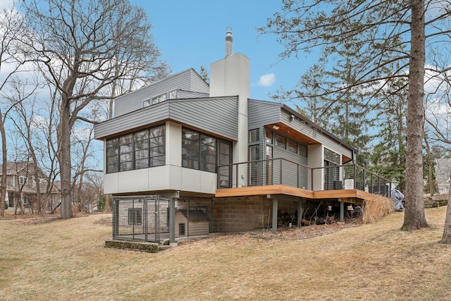 back of property featuring a lawn, a chimney, a wooden deck, and a sunroom