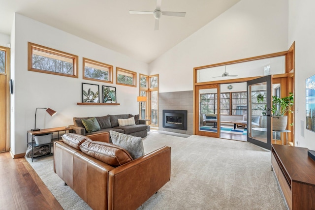 living area featuring high vaulted ceiling, ceiling fan, a tiled fireplace, and wood finished floors