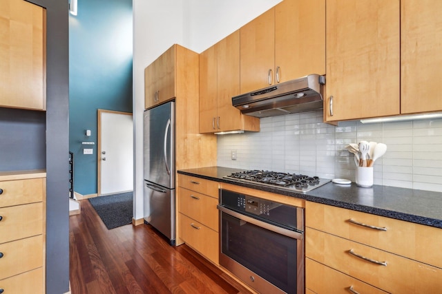 kitchen featuring under cabinet range hood, stainless steel appliances, decorative backsplash, dark wood-style floors, and light brown cabinetry