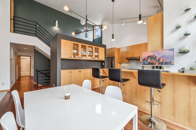 dining room with stairs, dark wood-style flooring, a towering ceiling, and track lighting