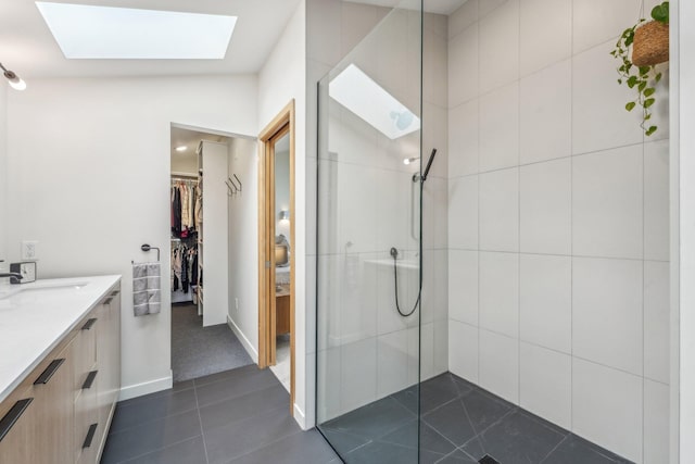 full bathroom with a skylight, a spacious closet, vanity, tile patterned flooring, and walk in shower