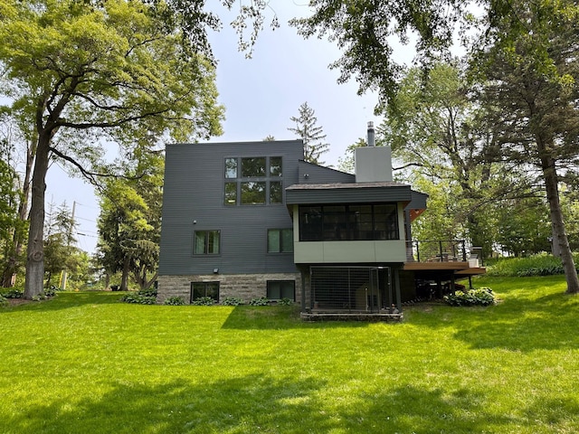 back of property featuring a lawn, a deck, a chimney, and a sunroom