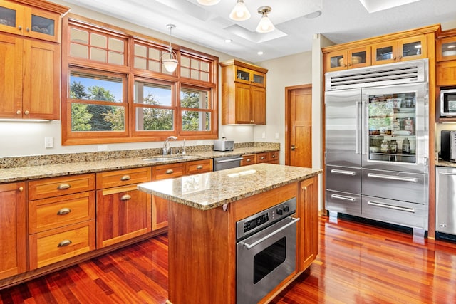 kitchen featuring glass insert cabinets, a center island, stainless steel appliances, pendant lighting, and a sink