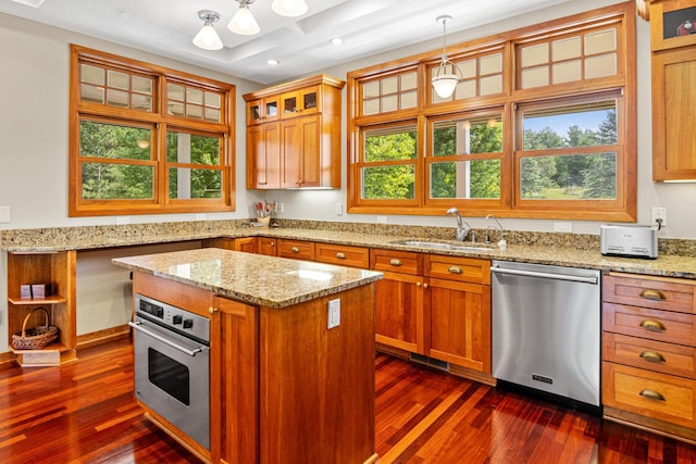 kitchen featuring light stone counters, pendant lighting, appliances with stainless steel finishes, glass insert cabinets, and a sink