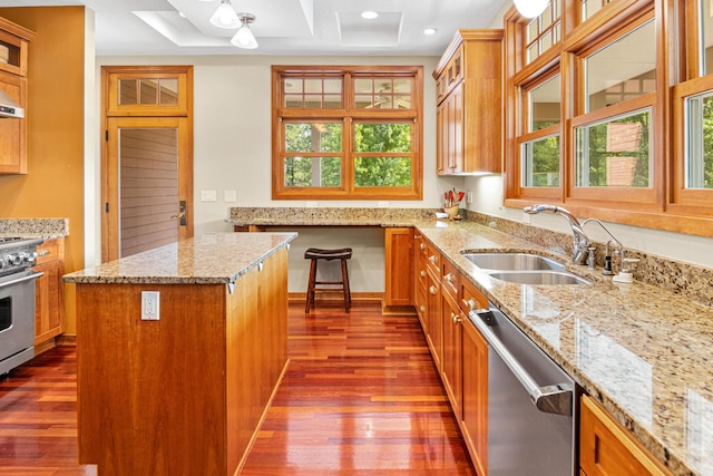 kitchen with appliances with stainless steel finishes, a sink, light stone counters, and a kitchen island