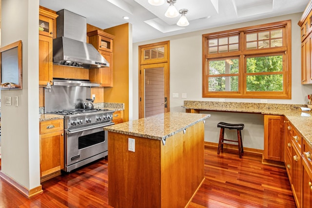 kitchen featuring wall chimney exhaust hood, a kitchen island, glass insert cabinets, light stone counters, and premium range