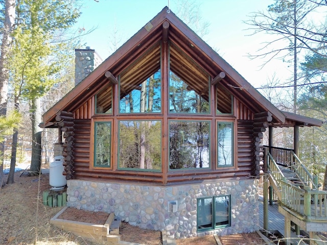 view of home's exterior featuring log exterior, stone siding, a sunroom, and a chimney