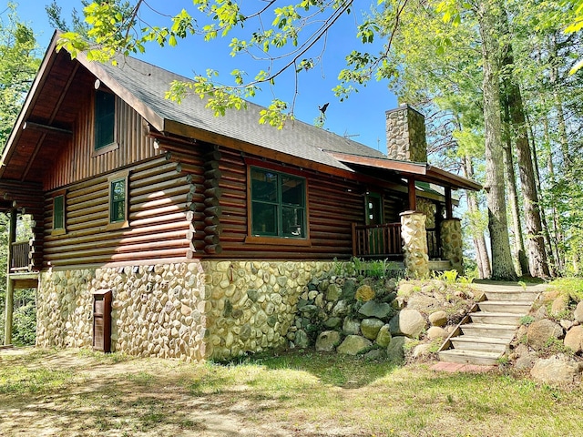 view of side of property featuring stone siding, log siding, stairs, and a chimney