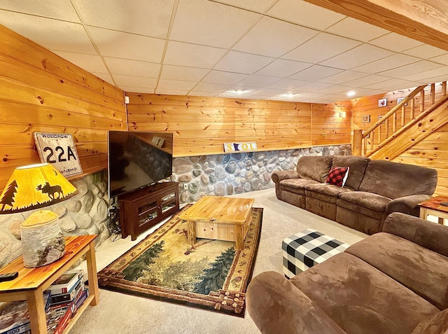 living room featuring carpet floors, wood walls, a drop ceiling, and stairway