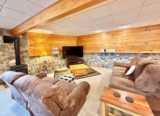 carpeted living area featuring a wood stove, wood walls, a paneled ceiling, and beam ceiling