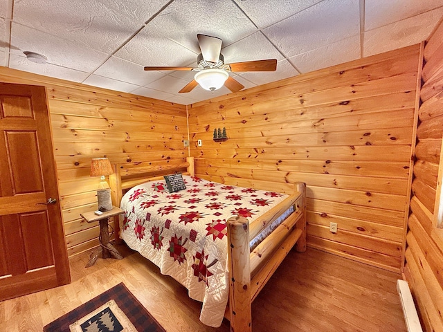 bedroom with light wood finished floors, wood walls, a ceiling fan, and a paneled ceiling