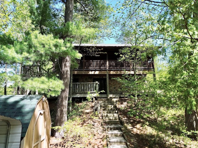 back of house featuring stairway, a deck, a shingled roof, an outbuilding, and a storage shed