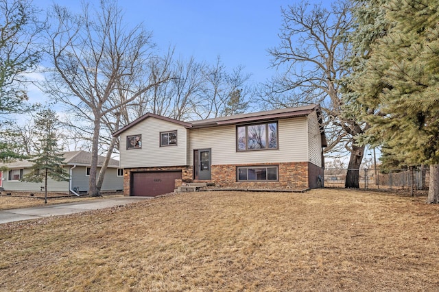 bi-level home featuring concrete driveway, brick siding, an attached garage, and fence