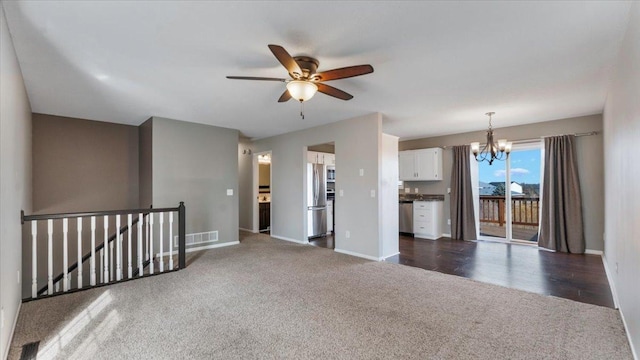 unfurnished room featuring ceiling fan with notable chandelier, dark colored carpet, visible vents, and baseboards