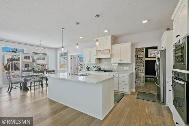 kitchen with stainless steel appliances, light countertops, white cabinets, a sink, and light wood-type flooring