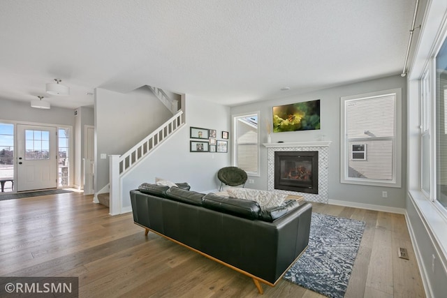 living room featuring a fireplace, wood-type flooring, a textured ceiling, baseboards, and stairs