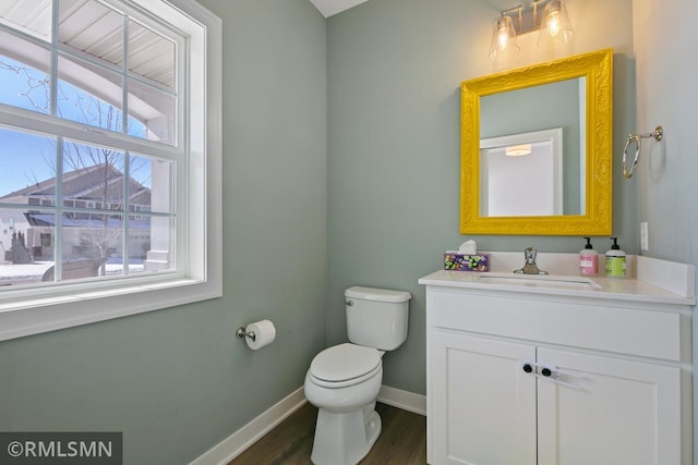 half bath featuring baseboards, vanity, toilet, and wood finished floors