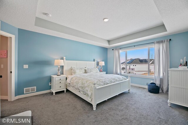 carpeted bedroom featuring a tray ceiling, visible vents, a textured ceiling, and baseboards