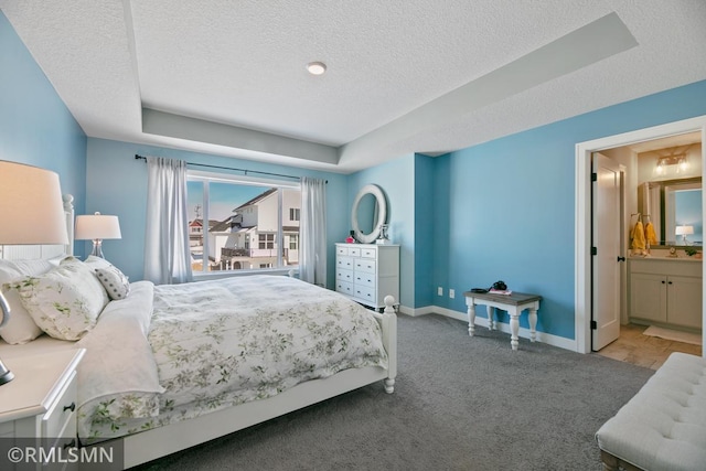 bedroom featuring a textured ceiling, ensuite bathroom, baseboards, a tray ceiling, and carpet