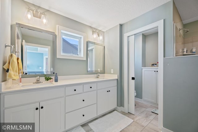 bathroom with a textured ceiling, double vanity, a sink, and toilet