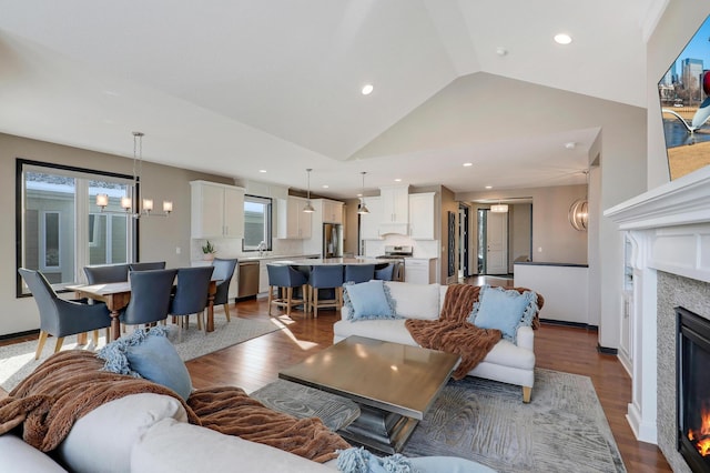 living area with dark wood-style floors, vaulted ceiling, a notable chandelier, and a glass covered fireplace