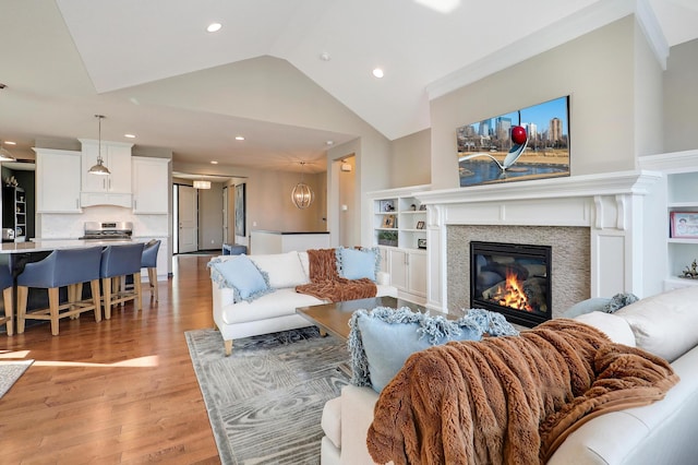 living room with lofted ceiling, recessed lighting, built in features, light wood-style floors, and a glass covered fireplace