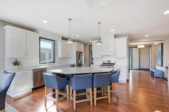 kitchen featuring a kitchen island, a kitchen breakfast bar, white cabinets, appliances with stainless steel finishes, and decorative light fixtures