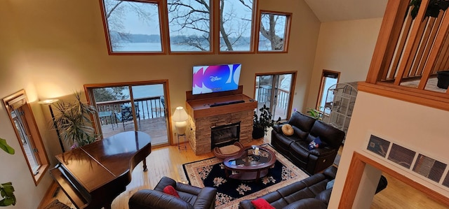 living room with a stone fireplace, a towering ceiling, wood finished floors, and visible vents
