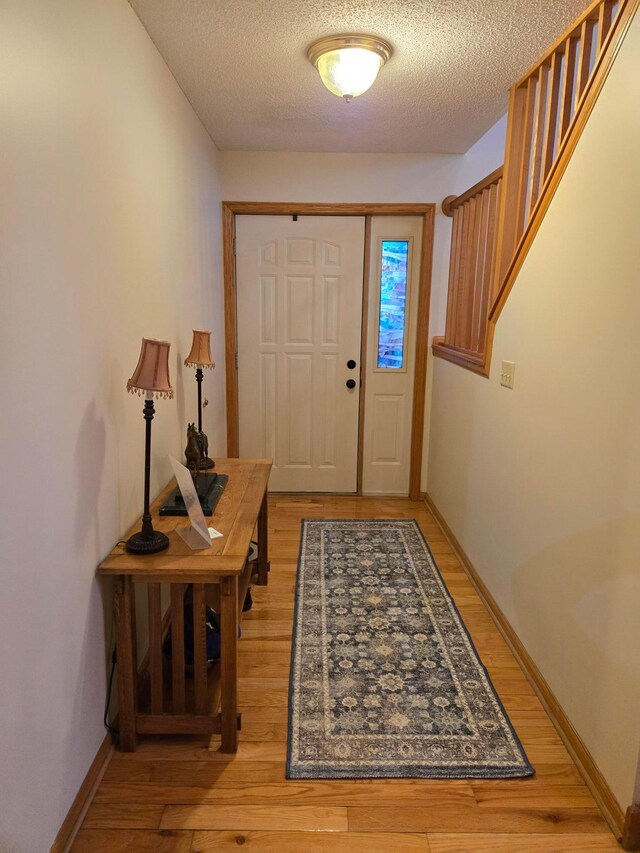 foyer entrance featuring light wood-style flooring, a textured ceiling, and baseboards