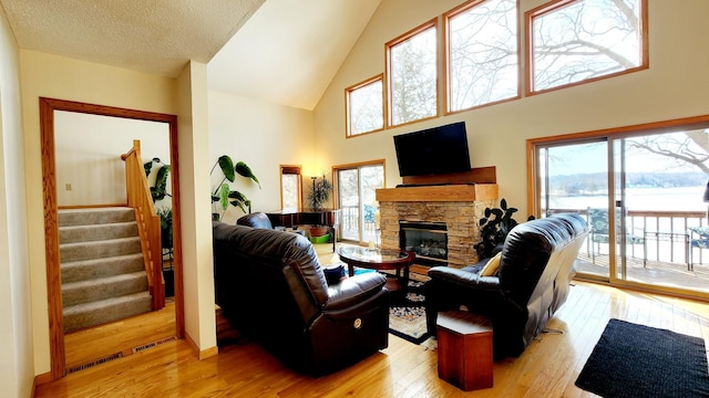 living area featuring light wood finished floors, a fireplace, high vaulted ceiling, and stairs