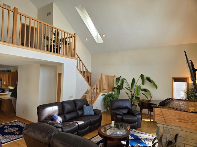 living room with a skylight, wood finished floors, high vaulted ceiling, and visible vents