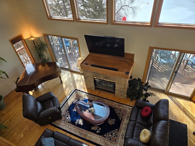 living room featuring a towering ceiling, a healthy amount of sunlight, a fireplace, and wood-type flooring