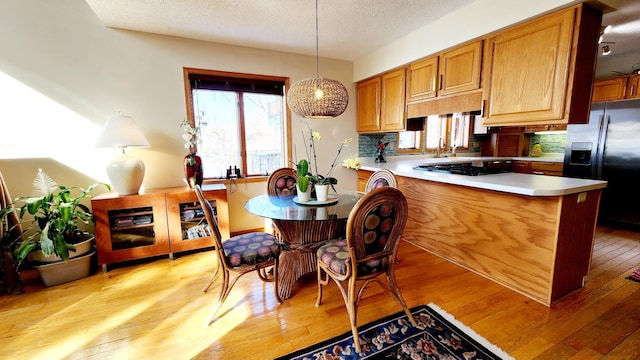 kitchen with light wood finished floors, light countertops, gas cooktop, a textured ceiling, and refrigerator with ice dispenser