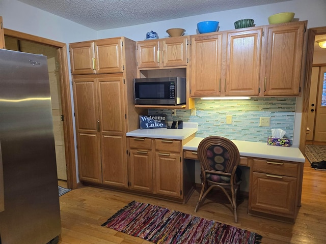 kitchen featuring stainless steel appliances, light wood-style flooring, light countertops, and backsplash