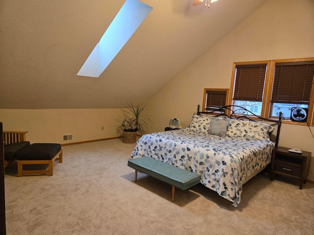 bedroom featuring lofted ceiling with skylight, ceiling fan, carpet floors, baseboards, and visible vents